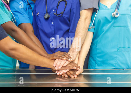Multiracial team of young doctors stacking hands indoor, Group Of Multiracial Doctor surgery team stacking hands in a operating room, medical teamwork. Stock Photo