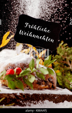 a black signboard with the text frohliche weihnachten, merry christmas in german, on a stollen cake sprinkled with icing sugar, placed on a wooden rus Stock Photo