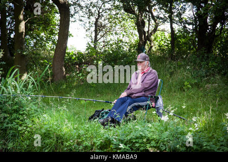 Man concentrates whilst fishing on the banks of the Coventry canal, Staffordshire, England Stock Photo