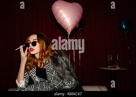 Flirty redhead at a party with a heart shaped balloon in the background Stock Photo