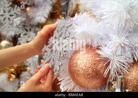 Female's Hands Decorating Christmas Tree with a Glitter Snowflake Shaped Ornament Stock Photo