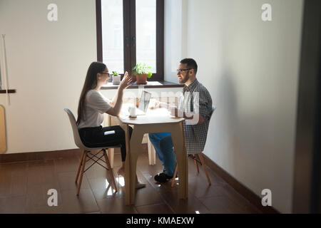 Coworkers sitting at meeting and discussing new concept in work. Two smiling millennial employees talking about business plan and success result in of Stock Photo