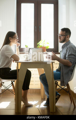 Young businesswoman and businessman sitting at meeting and discussing new working concept. Millennial employees negotiating in office. Vertical image Stock Photo
