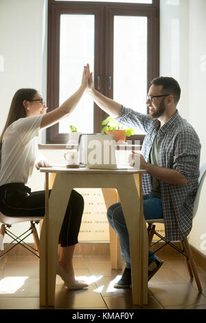 Millennial colleagues giving high fives while finishing working project in business office. Two happy successful young managers, winning concept. Vert Stock Photo
