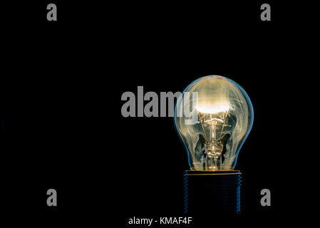 Horizontal photo of single glass bulb placed in the socket on black background. The fire and flame inside is caused by burning wire. The bright smoke  Stock Photo