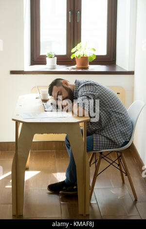 Fatigued casual businessman tired from hard working routine and fell asleep at workplace over laptop. Stressful overworked job on Monday. Vertical ima Stock Photo