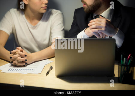 Bearded businessman in suit explaining new working project to female coworker. Businessman and businesswoman sitting at desktop with laptop in office Stock Photo