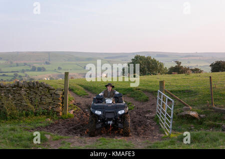 A young boy riding a quad on farm land coming through a farm gate on an evening in September in Weardale in County Durham while out on a hunting trip. Stock Photo