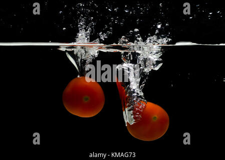 Two cherry tomatoes falling into splashing water isolated on black background. Stock Photo
