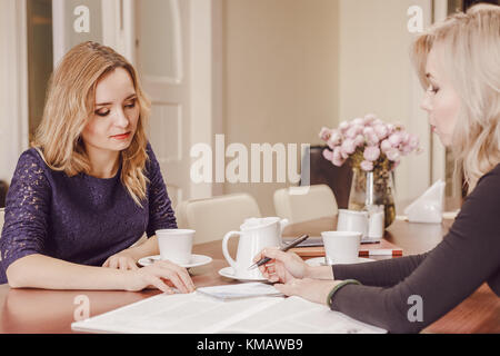 Two young women discussing documents and drinking tea at meeting in conference room Stock Photo