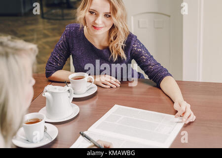 Two young women discussing documents and drinking tea at meeting in conference room Stock Photo