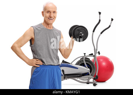 Senior exercising with a dumbbell in front of a cross training machine and a pilates ball isolated on white background Stock Photo