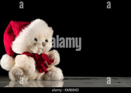 Small stuffed white bear sitting on a reflective surface, black background Stock Photo
