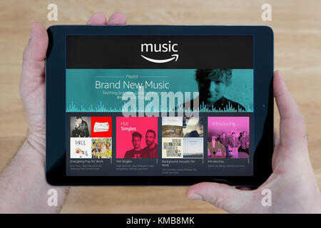 A man looks at the Amazon Music website on his iPad tablet device, shot against a wooden table top background (Editorial use only) Stock Photo