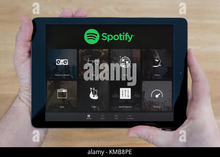 A man looks at the Spotify app on his iPad tablet device, shot against a wooden table top background (Editorial use only) Stock Photo