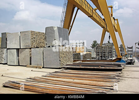 Heavy natural granite stone blocks stacked for processing into floor and wall tiles and slabs by cutting and polishing with the help of gantry crane Stock Photo