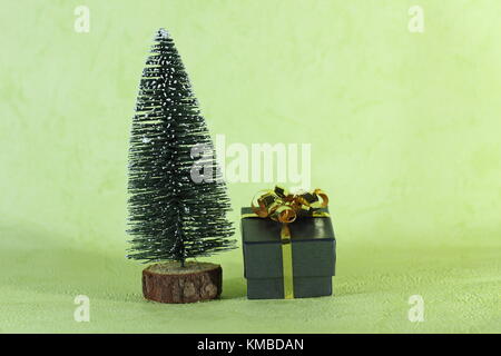 a small gift placed next to a Christmas tree decorative and miniature on green background Stock Photo