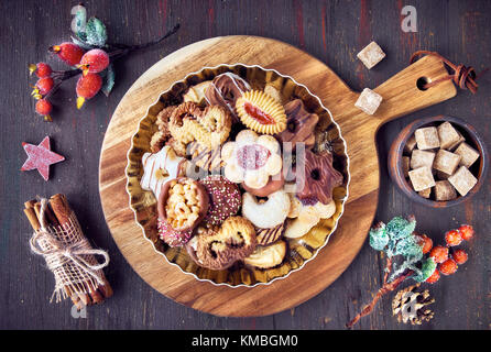Plate of Christmas cookies on a wooden board on dark rustic background with decorations and ingredients around Stock Photo