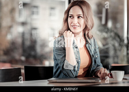 Cute cheerful woman looking into the distance while being in a cafe Stock Photo