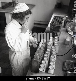 1950s, historical, female lab technician drawing up milk from a bottle with a straw to make test tube samples for checking. Stock Photo