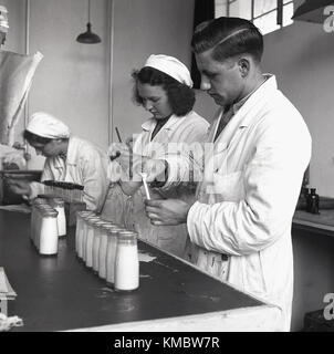 1950s, historical, male and female lab technicians in white coats working at a diary checking samples of milk taken from milk bottles. Stock Photo