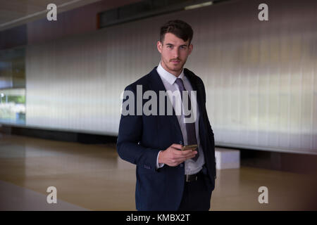 Portrait confident, serious businessman texting with smart phone in office lobby Stock Photo