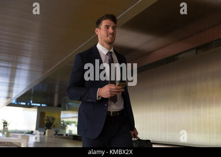 Businessman walking with smart phone in office lobby Stock Photo