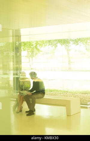 Silhouette businessman and businesswoman talking on bench in modern office Stock Photo