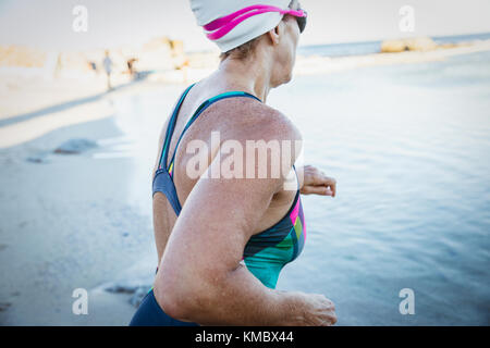 Female open water swimmer running into ocean Stock Photo
