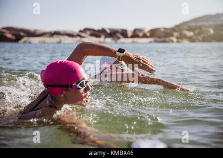 Determined female open water swimmer with smart watch swimming in sunny ocean Stock Photo