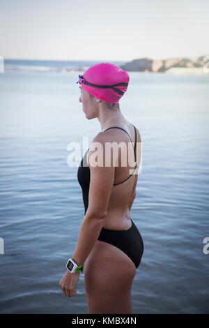 Pensive female open water swimmer with smart watch wading in ocean surf Stock Photo