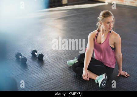 Young woman stretching, twisting in gym next to dumbbells Stock Photo