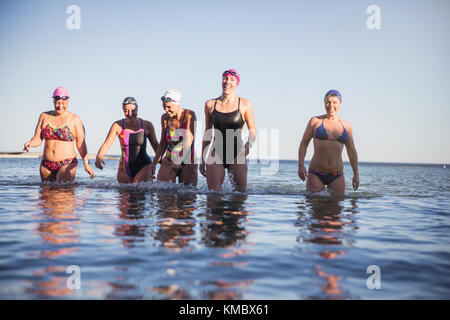 Smiling female open water swimmers wading in ocean surf Stock Photo