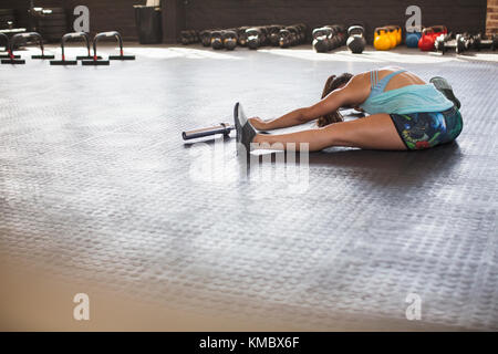 Young woman stretching, doing forward fold using barbell in gym Stock Photo