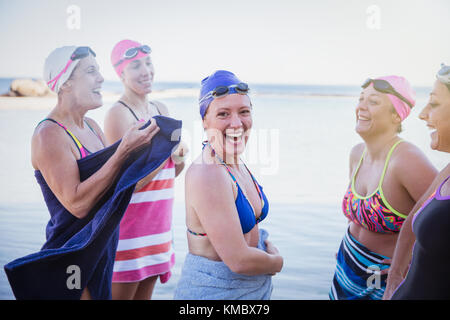 Portrait smiling female open water swimmers drying off with towels in ocean Stock Photo