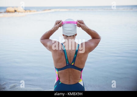 Female open water swimmer adjusting swimming goggles at ocean Stock Photo