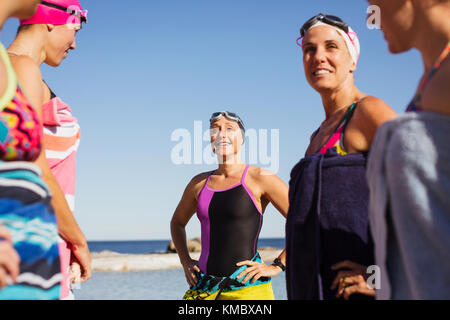 Smiling female open water swimmers wrapped din towels on sunny beach Stock Photo