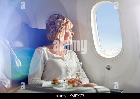 Smiling woman drinking champagne,traveling first class,looking out airplane window Stock Photo