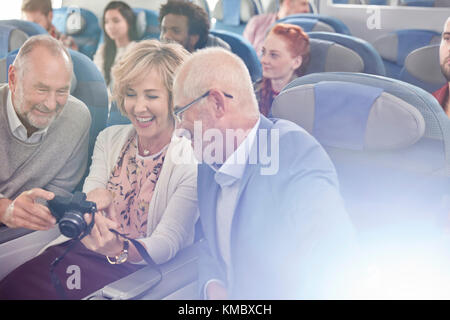 Smiling friends looking at photos on digital camera on airplane Stock Photo