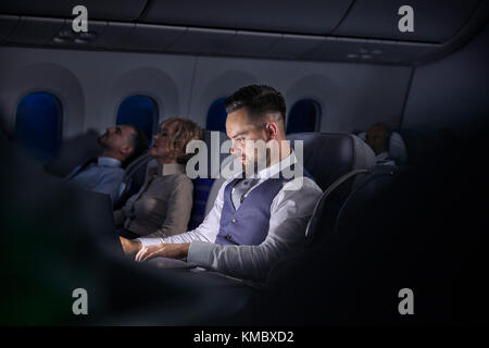 Businessman working on laptop on night airplane Stock Photo