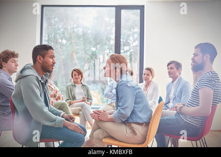 Group watching man and woman talking face to face in group therapy session Stock Photo