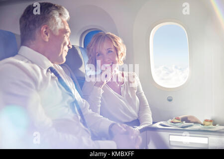 Smiling mature couple eating and talking in first class on airplane Stock Photo