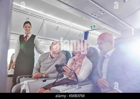 Friends looking at photos on digital camera on airplane Stock Photo