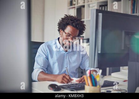 Businessman taking notes at computer in office Stock Photo