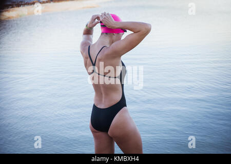 Female open water swimmer adjusting swimming goggles at ocean Stock Photo