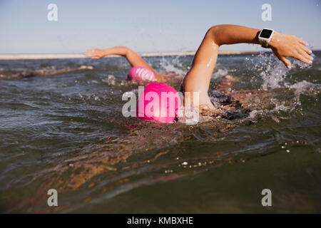 Female open water swimmer with smart watch swimming in sunny ocean Stock Photo