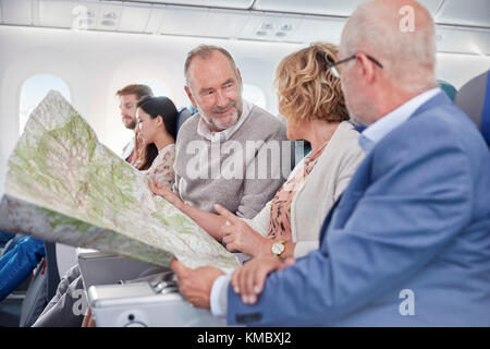 Mature friends looking at map on airplane Stock Photo
