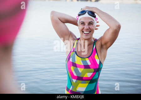 Portrait laughing, smiling female open water swimmer adjusting swimming cap in ocean Stock Photo