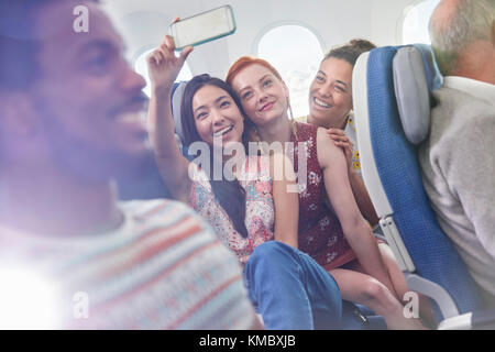 Young women friends with camera phone taking selfie on airplane Stock Photo