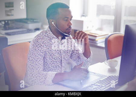 Male graphic designer working at computer in graphics tablet,talking on telephone with headphones Stock Photo